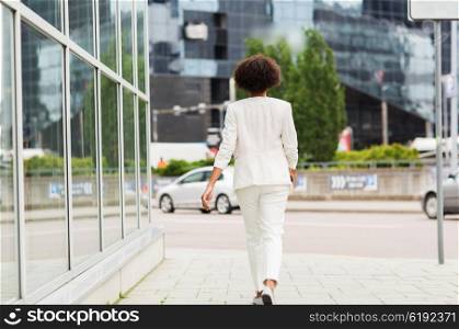 business and people concept - young african american businesswoman walking in city. african american businesswoman walking in city