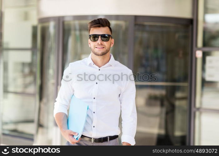 business and people concept - young man in sunglasses with folder on city street. young man with business file on city street