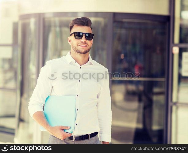 business and people concept - young man in sunglasses with folder on city street. young man with business file on city street