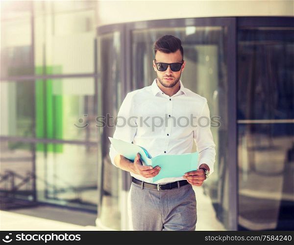 business and people concept - young man in sunglasses with folder on city street. young man with business file on city street
