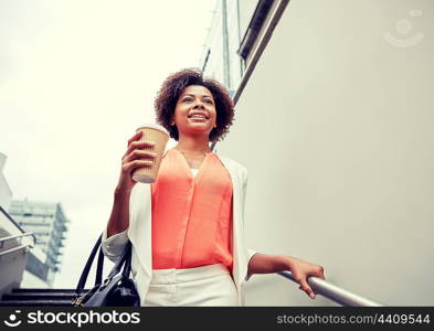 business and people concept - young smiling african american businesswoman with coffee cup going down stairs into city underpass. happy african businesswoman with coffee in city