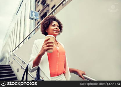 business and people concept - young smiling african american businesswoman with coffee cup going down stairs into city underpass. happy african businesswoman with coffee in city