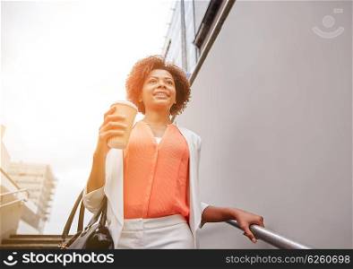 business and people concept - young smiling african american businesswoman with coffee cup going down stairs into city underpass. happy african businesswoman with coffee in city