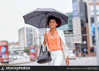 business and people concept - young smiling african american businesswoman with umbrella and handbag walking down city street. happy african american businesswoman with umbrella