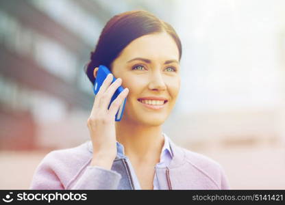 business and people concept - young smiling businesswoman calling on smartphone over office building. young smiling businesswoman calling on smartphone