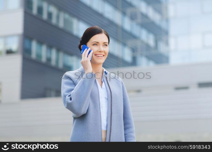 business and people concept - young smiling businesswoman calling on smartphone over office building. young smiling businesswoman calling on smartphone