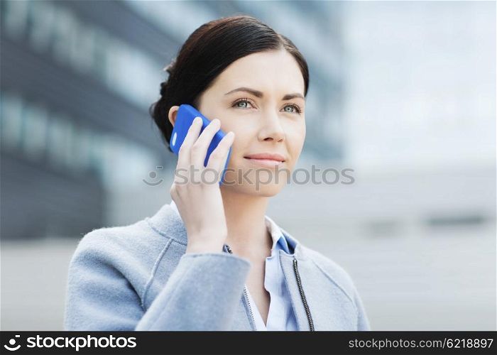 business and people concept - young smiling businesswoman calling on smartphone over office building. young smiling businesswoman calling on smartphone