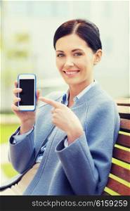 business and people concept - young smiling businesswoman showing smartphone blank screen and sitting on city bench. young smiling businesswoman showing smartphone