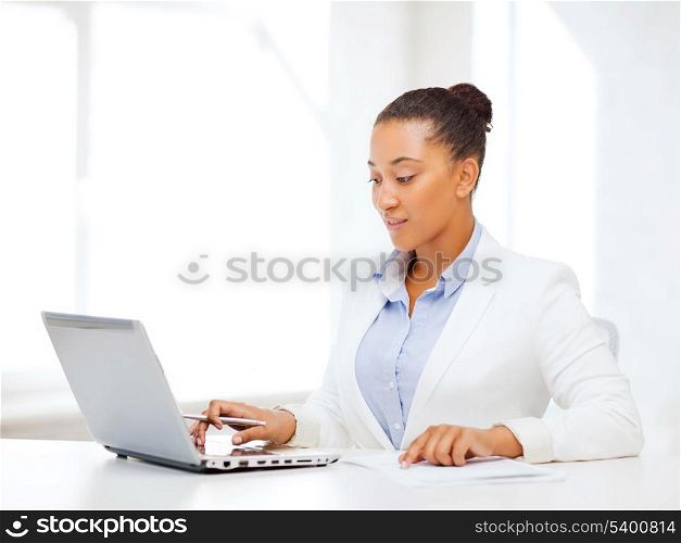 business and technology concept - african businesswoman with laptop writing something in notebook