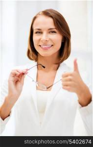 business and vision correction concept - businesswoman with eyeglasses showing thumbs up in office