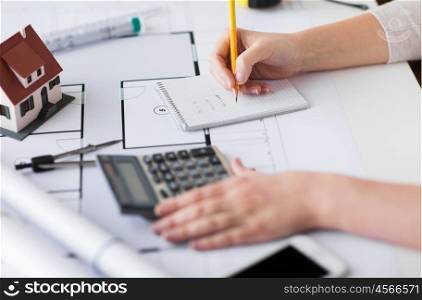 business, architecture, building, construction and people concept - close up of architect hand with blueprint and architectural tools writing to notebook
