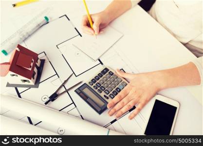 business, architecture, building, construction and people concept - close up of architect hand with blueprint counting on calculator. close up of architect hand counting on calculator