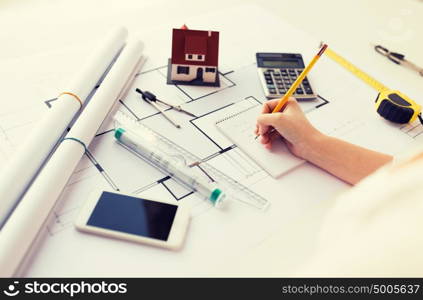 business, architecture, building, construction and people concept - close up of architect hand with blueprint and architectural tools writing to notebook. close up of hand on blueprint writing to notebook