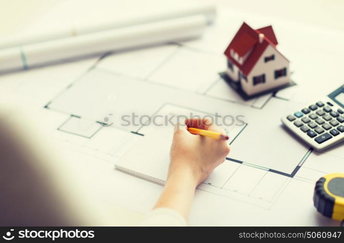 business, architecture, building, construction and people concept - close up of architect hand with blueprint and architectural tools writing to notebook. close up of hand on blueprint writing to notebook