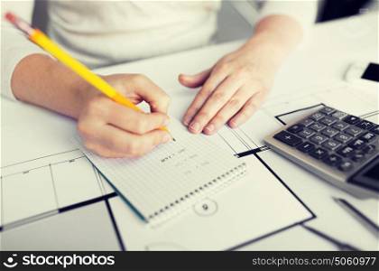 business, architecture, building, construction and people concept - close up of architect hand with blueprint and calculator writing to notebook. close up of architect hand writing to notebook