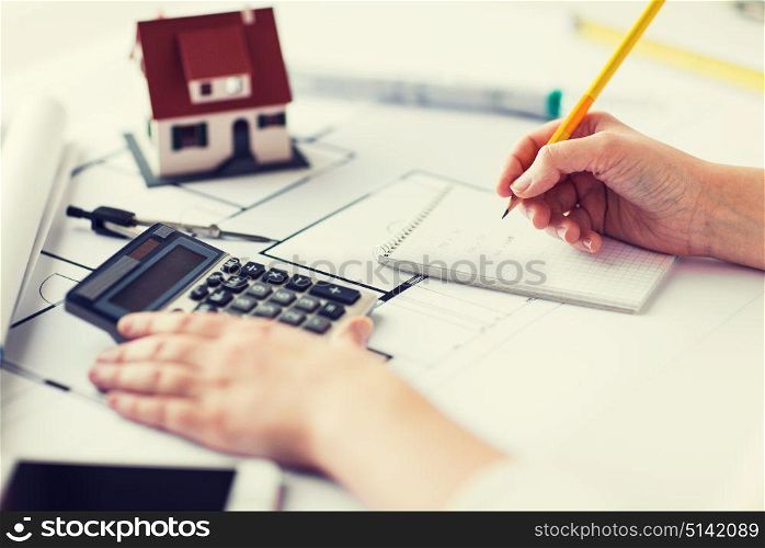 business, architecture, building, construction and people concept - close up of architect hand with blueprint and architectural tools writing to notebook. close up of hand on blueprint writing to notebook