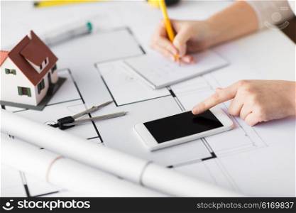business, architecture, building, construction and people concept - close up of architect hand with living house blueprint and smarphone writing to notebook