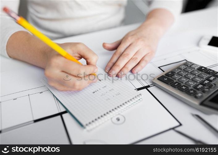 business, architecture, building, construction and people concept - close up of architect hand with blueprint and calculator writing to notebook