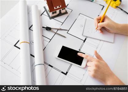 business, architecture, building, construction and people concept - close up of architect hand with living house blueprint and smarphone writing to notebook