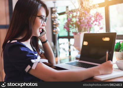 Business Asian woman hold pick up Smartphone working with laptop computer on in coffee shop like the background.