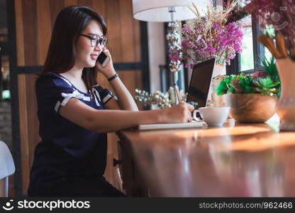 Business Asian woman hold pick up Smartphone working with laptop computer on in coffee shop like the background.