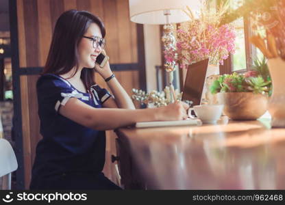 Business Asian woman hold pick up Smartphone working with laptop computer on in coffee shop like the background.