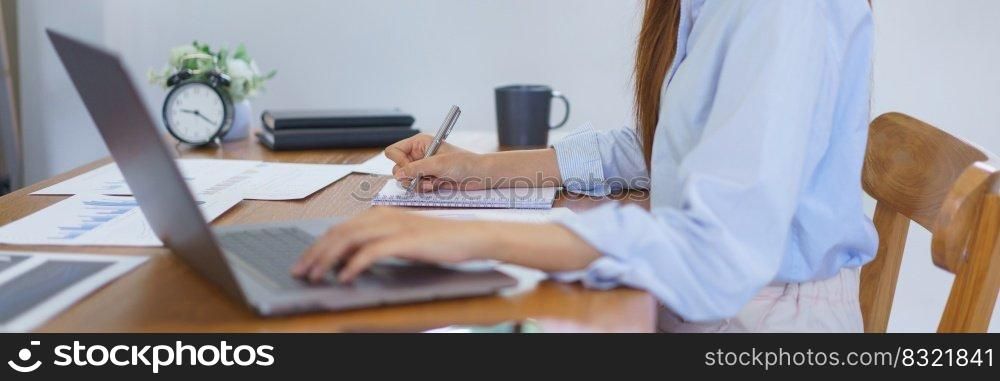 Business at home concept, Businesswoman is reading marketing plan data on laptop and taking notes.