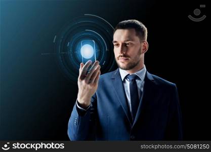 business, augmented reality and future technology concept - businessman in suit working with transparent smartphone and hologram over black background. businessman with transparent smartphone