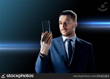 business, augmented reality and future technology concept - businessman in suit working with transparent smartphone over black background. businessman with transparent smartphone