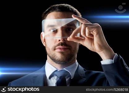 business, augmented reality and future technology concept - businessman in suit working with transparent smartphone over black background. businessman with transparent smartphone