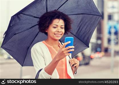 business, bad weather and people and concept - happy african american businesswoman with umbrella texting on smartphone at city street