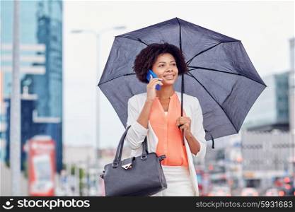 business, bad weather and people and concept - happy african american businesswoman with umbrella and handbag calling on smartphone at city street