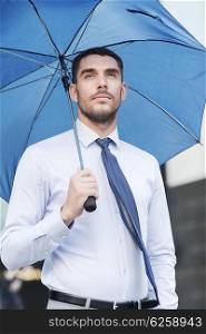 business, bad weather and people and concept - young serious businessman with umbrella outdoors