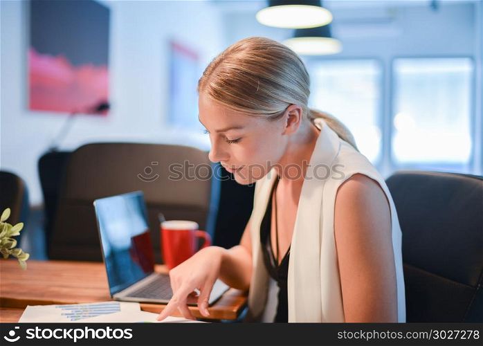 Business blonde girl drinking a cup of coffee in front of a lapt. Business blonde girl drinking a cup of coffee in front of a laptop. Business blonde girl drinking a cup of coffee in front of a laptop