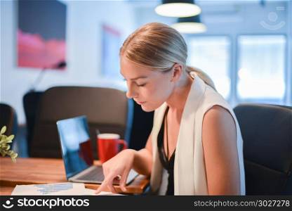 Business blonde girl drinking a cup of coffee in front of a lapt. Business blonde girl drinking a cup of coffee in front of a laptop. Business blonde girl drinking a cup of coffee in front of a laptop