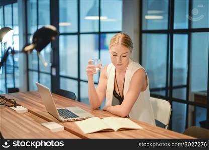Business blonde girl drinking water in front of a laptop
