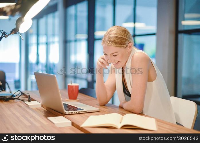 Business blonde girl writing a book and phoning in front of a la. Business blonde girl writing a book and phoning in front of a laptop. Business blonde girl writing a book and phoning in front of a laptop