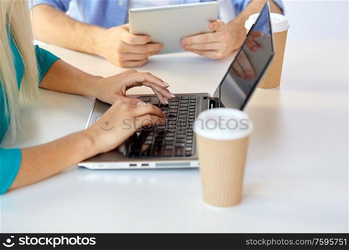 business, break and people concept - close up of woman typing on laptop and coffee cups on table. woman typing on laptop and coffee cups on table