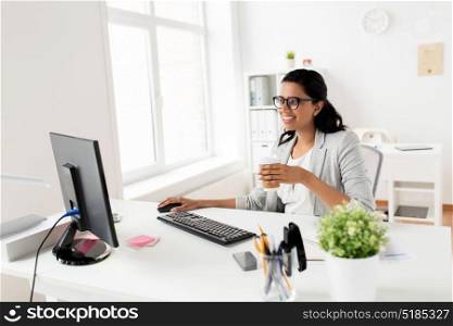business, break and people concept - smiling businesswoman drinking coffee or tea sitting at office table. businesswoman drinking coffee or tea at office