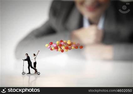 Business break. Businessman and businesswoman riding scooter with balloons in hand