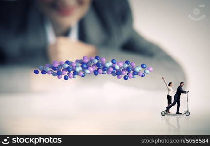 Business break. Businessman and businesswoman riding scooter with balloons in hand