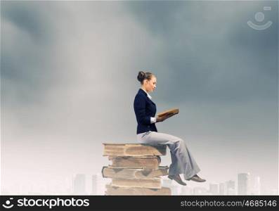 Business break. Young attractive businesswoman sitting on pile of old books reading