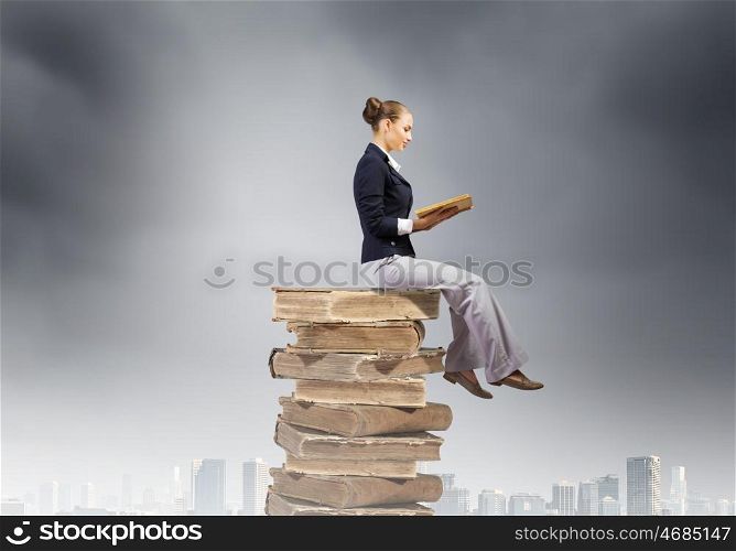 Business break. Young attractive businesswoman sitting on pile of old books reading