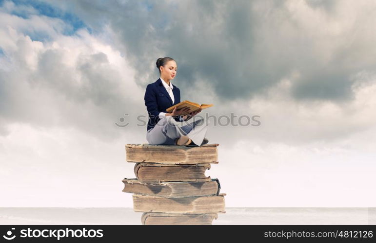 Business break. Young attractive businesswoman sitting on pile of old books reading