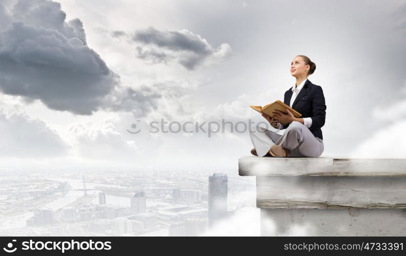 Business break. Young attractive businesswoman sitting on roof of building and reading book