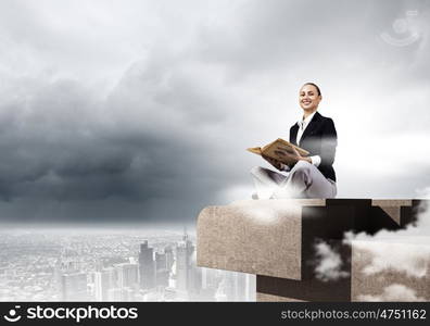 Business break. Young attractive businesswoman sitting on roof of building and reading book