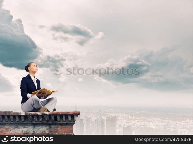 Business break. Young attractive businesswoman sitting on roof of building and reading book
