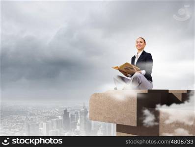 Business break. Young attractive businesswoman sitting on roof of building and reading book
