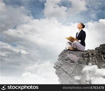 Business break. Young attractive businesswoman sitting on top of rock and reading