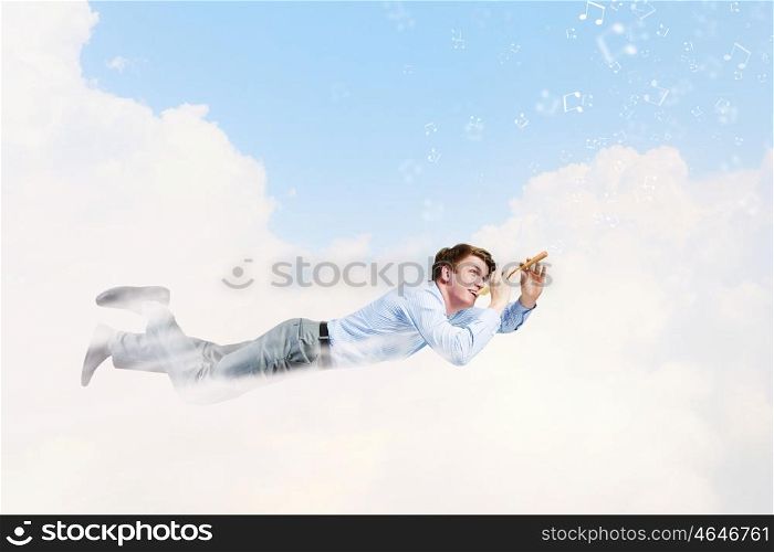 Business break. Young businessman flying in sky and playing fife